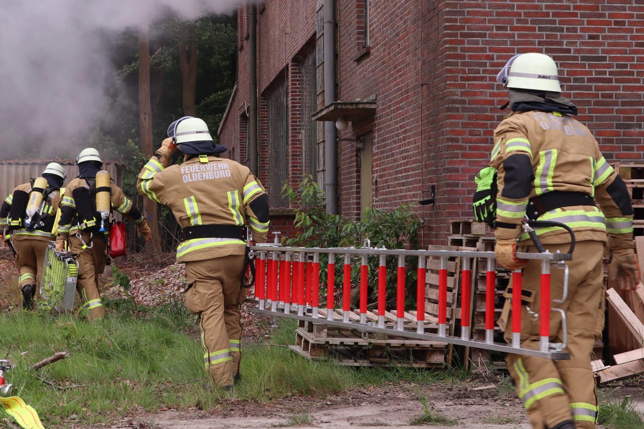 Nur eine Übung: Kameradinnen und Kameraden der Feuerwehr Oldenburg tragen Leitern zu einem brennenden Gebäude.